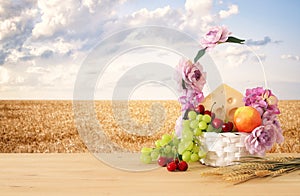 Image of fruits and cheese in decorative basket with flowers over wooden table. Symbols of jewish holiday - Shavuot.
