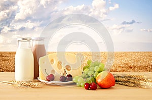 Image of fruits and cheese in decorative basket with flowers over wooden table. Symbols of jewish holiday - Shavuot.