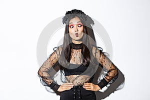 Image of funny asian girl celebrating halloween, wearing gothic lace dress to impersonate witch, showing silly faces and