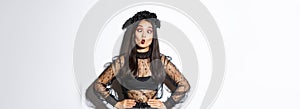 Image of funny asian girl celebrating halloween, wearing gothic lace dress to impersonate witch, showing silly faces and