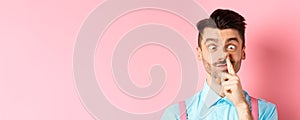 Image of funny caucasian guy picking nose and squint eyes, making dumb face, standing on pink background