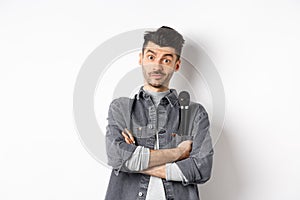 Image of funny male entertainer or singer, holding microphone in pocket of jacket and look at camera with arms crossed