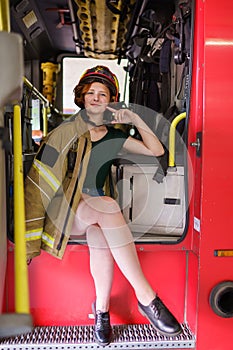 Image of ginger firewoman in helmet looking in camera sitting in cab of fire engine