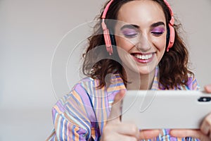 Image of ginger happy woman using cellphone and wireless headphones