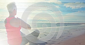 Image of glowing light over senior woman practicing yoga by seaside