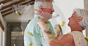 Image of gold confetti falling over happy caucasian senior couple dancing at home