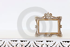 Image of gold tone baroque vintage empty photo frame over wooden table. For mockup, can be used for photography montage