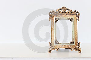 Image of gold tone baroque vintage empty photo frame over wooden table. For mockup, can be used for photography montage