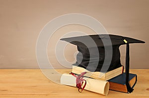 Image of graduation black hat over old books next to graduation on wooden desk. Education and back to school concept.