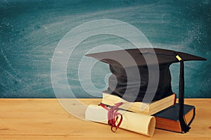 Image of graduation black hat over old books next to graduation on wooden desk. Education and back to school concept.