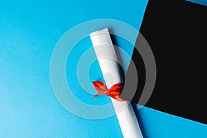 Image of graduation hat and diploma on blue surface