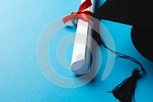 Image of graduation hat and diploma on blue surface