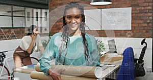 Image of graphs and icons over smiling biracial woman standing and holding cardboard rolls