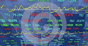 Image of graphs and trading board moving over desktops and keyboards on desk at office