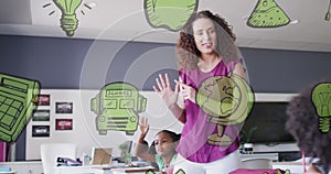 Image of green school icons over happy diverse pupils and female teacher talking in class