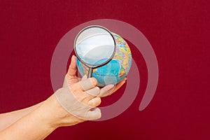 Image of a hand holding a magnifying glass over an world globe