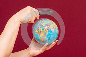 Image of a hand holding a magnifying glass over an world globe