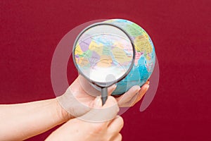 Image of a hand holding a magnifying glass over an world globe