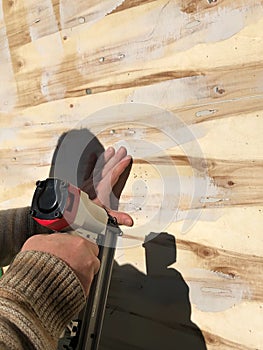 Image of the hands of a man who uses a pneumatic nailer to drive nails into plywood