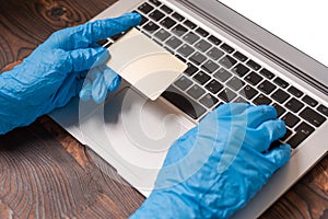 Image of hands in medical gloves on the background of a laptop. The woman holds a plastic bank card and enters the number on the