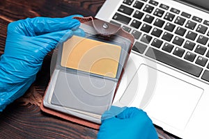 Image of hands in medical gloves on the background of a laptop. The woman holds a plastic bank card and enters the number on the