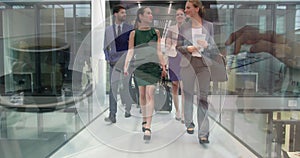 Image of hands of woman using laptop over happy colleagues walking in modern building