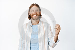 Image of handsome blond man showing credit card and smiling pleased, paying contactless, making purchase in store