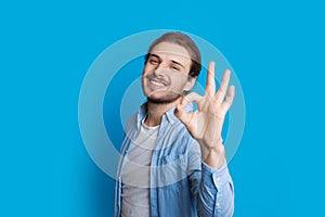 Image of a Handsome caucasian boy gesturing approbation sign while smiling and posing on a blue background
