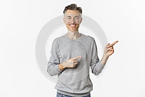 Image of handsome middle-aged man showing something on copy space, pointing fingers right and smiling, standing over