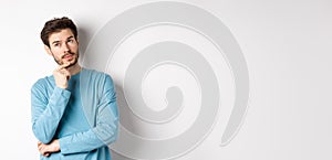 Image of handsome young man making choice, thinking and looking pensive up, standing over white background