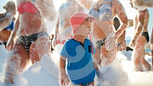 Image of happy 3 years old toddler boy with young mother having fun and dancing on the beach soap foam disco party