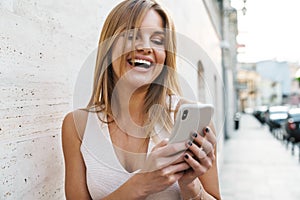 Image of happy blonde woman laughing and using mobile phone