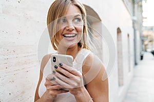 Image of happy blonde woman smiling and using mobile phone