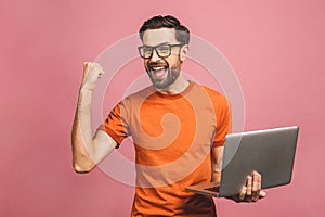 Image of happy excited young man posing isolated over pink background wall using laptop computer make winner gesture