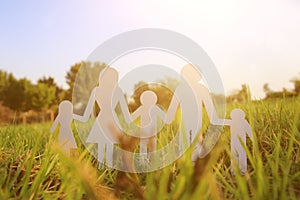 Image of happy family concept. paper cut people holding hands together in green grass during sunset.