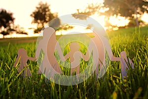 Image of happy family concept. paper cut people holding hands together in green grass during sunset.