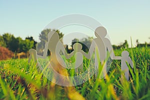 Image of happy family concept. paper cut people holding hands together in green grass during sunset.