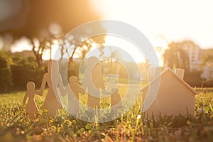 Image of happy family concept. wooden cut people holding hands together next to home in green grass during sunset.
