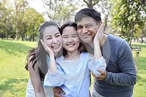 Image of happy family, daughter putting her hands on parents cheek with smiling during summer time in the park