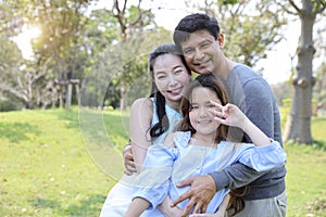 Image of happy family, daughter showing victory symbol on her hands with smiling during summer time in the park