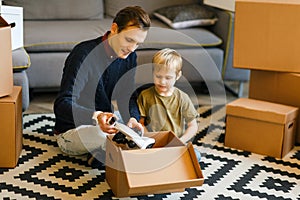 Image of happy father and son with microscope sitting on floor among cardboard boxes