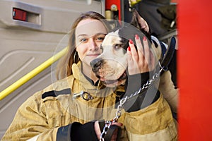 Image of happy firewoman with dog standing near fire truck