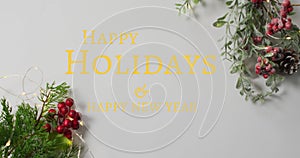 Image of happy holidays christmas text over decorations on grey background