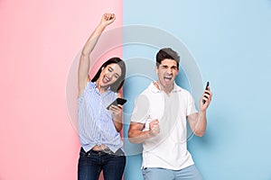 Image of happy man and woman wearing earphones listening to music on smartphones, isolated over colorful background