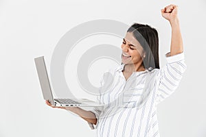 Image of happy pregnant woman 30s with big belly smiling and holding laptop in hands