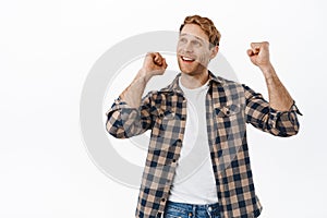 Image of happy redhead man celebrating sport victory, dancing and looking up as if watching sports game on screen above