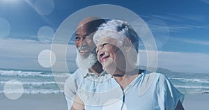 Image of happy senior african american couple embracing at beach over light spots