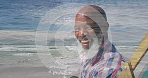 Image of happy senior african american man sitting at beach over sea