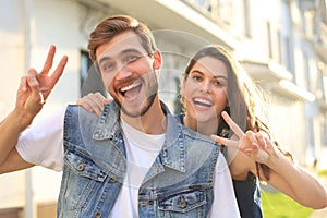 Image of a happy smiling cheerful young couple outdoors take a selfie by camera showing peace