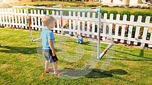 Image of happy smiling toddler boy scoring goal on football field at park. Active children doings sports